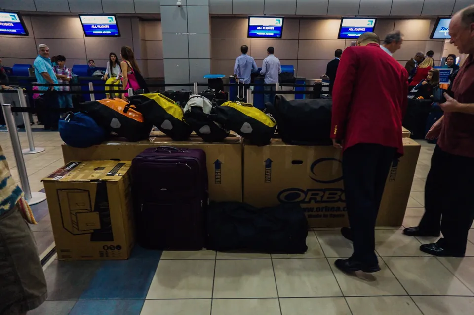 Bike boxes and stacked yellow and orange panniers at an airline check-in desk.
