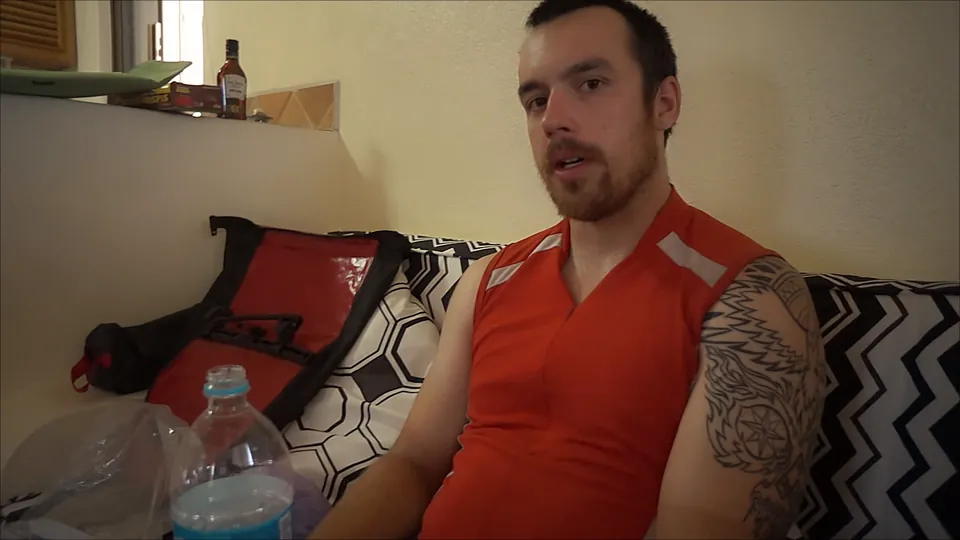 A rider in a red jersey sitting on a hotel bed, explaining his symptoms to camera.