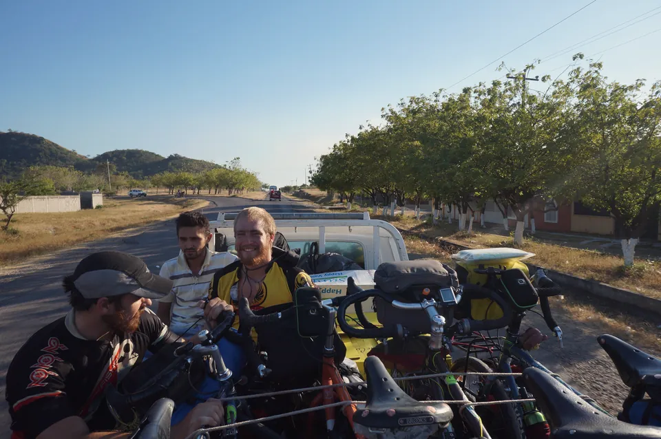 Riders and a local passenger in the back of a pickup truck crammed with bicycles.