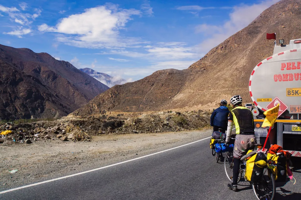 Two riders tucked in behind a fuel tanker on a dry mountain road in Peru.